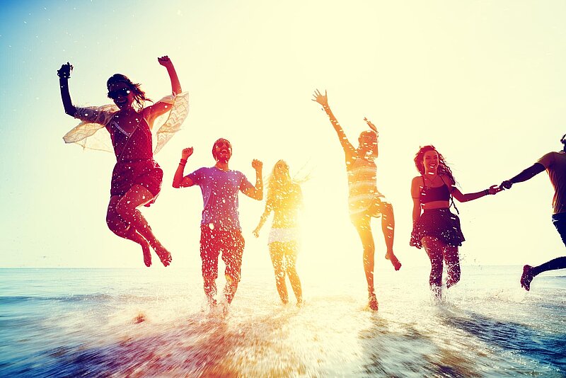 Gruppe von Freunden, die an einem sonnigen Tag in seichtem Wasser am Strand unterwegs ist