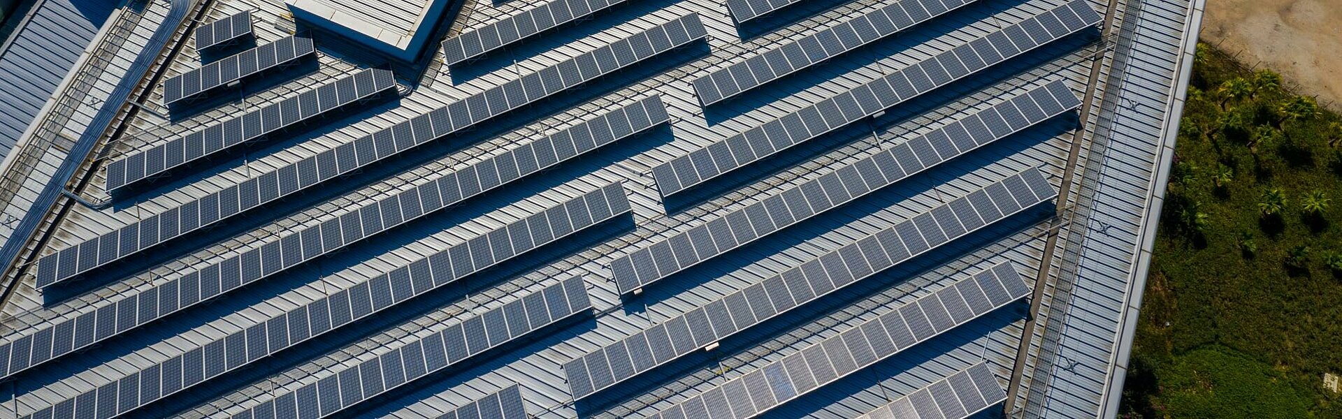 Luftaufnahme von Reihen mit Photovoltaikmodulen auf dem Flachdach einer Gewerbehalle