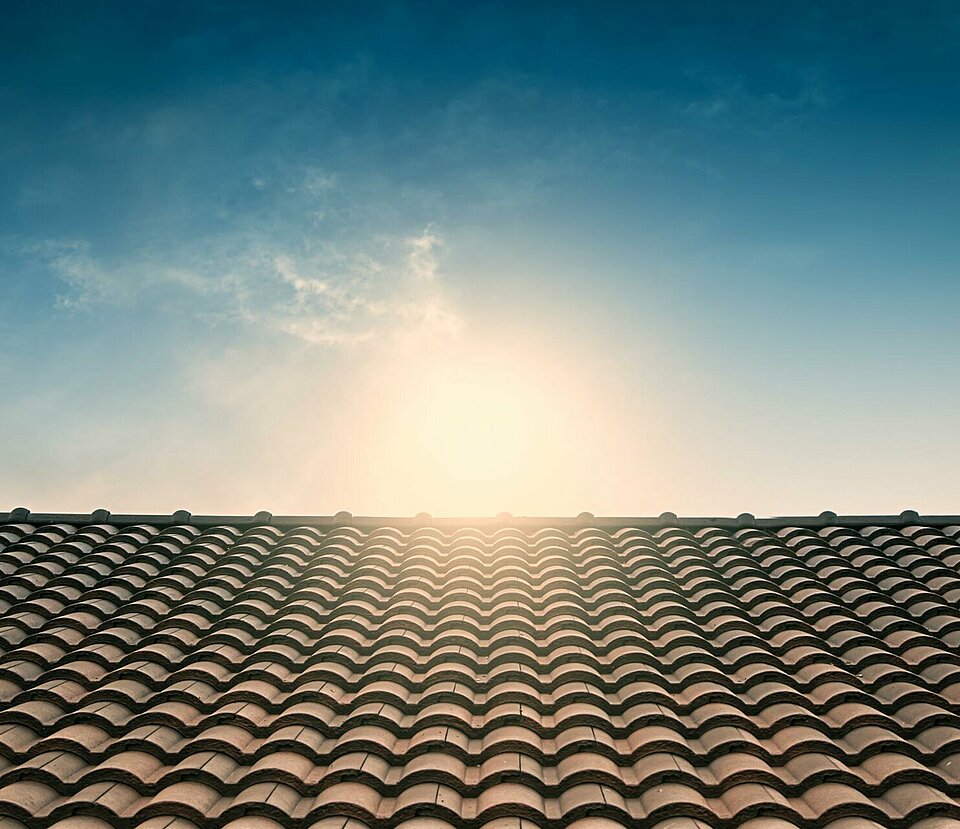 Sonne über einem mit Schindeln bedeckten Dach als Symbolbild für Dachausrichtung