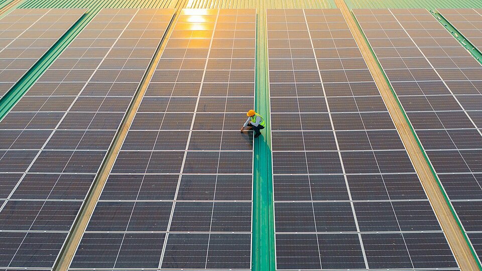 Techniker kontrolliert nach der Installation Photovoltaikmodule auf dem weitläufigen Flachdach einer Industriehalle