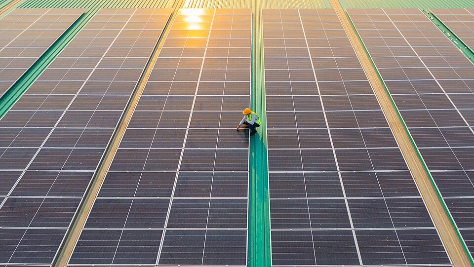 Techniker kontrolliert nach der Installation Photovoltaikmodule auf dem weitläufigen Flachdach einer Industriehalle